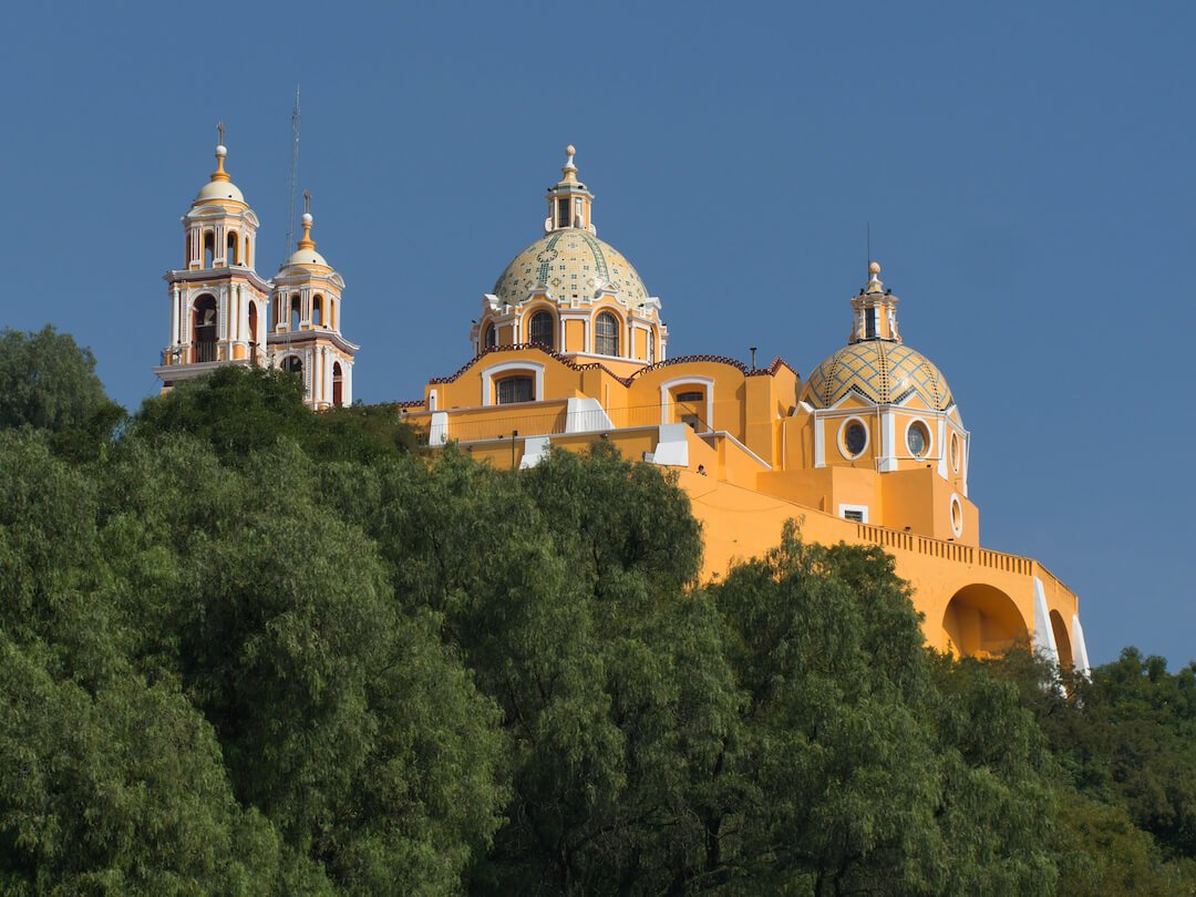 A yellow church with multiple domes appears above a forest of trees