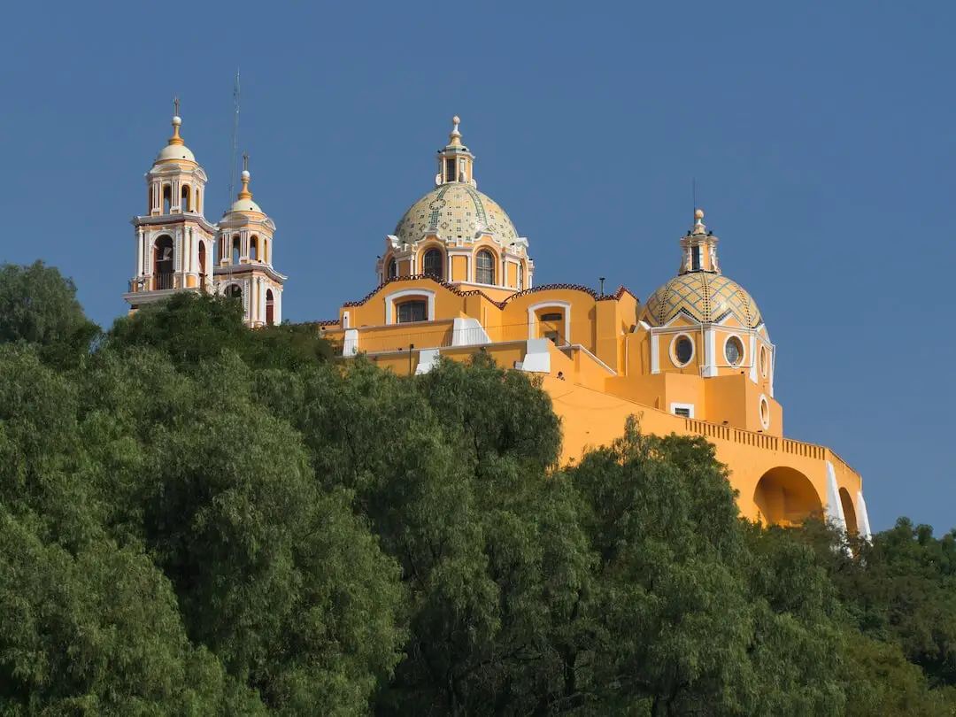 Iglesia de NuestraSenora de los Remedios - Cholula A yellow church with multiple domes appears above a forest of trees