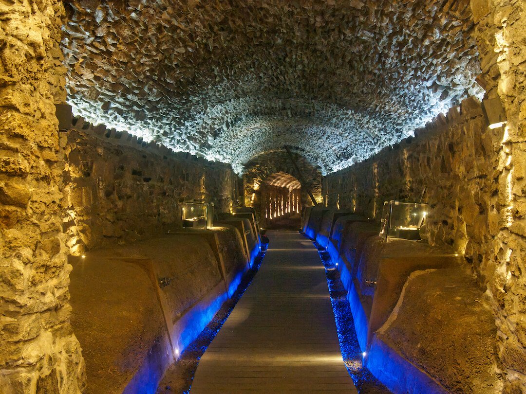 An underground stone tunnel illuminated with blue light to show the pathway