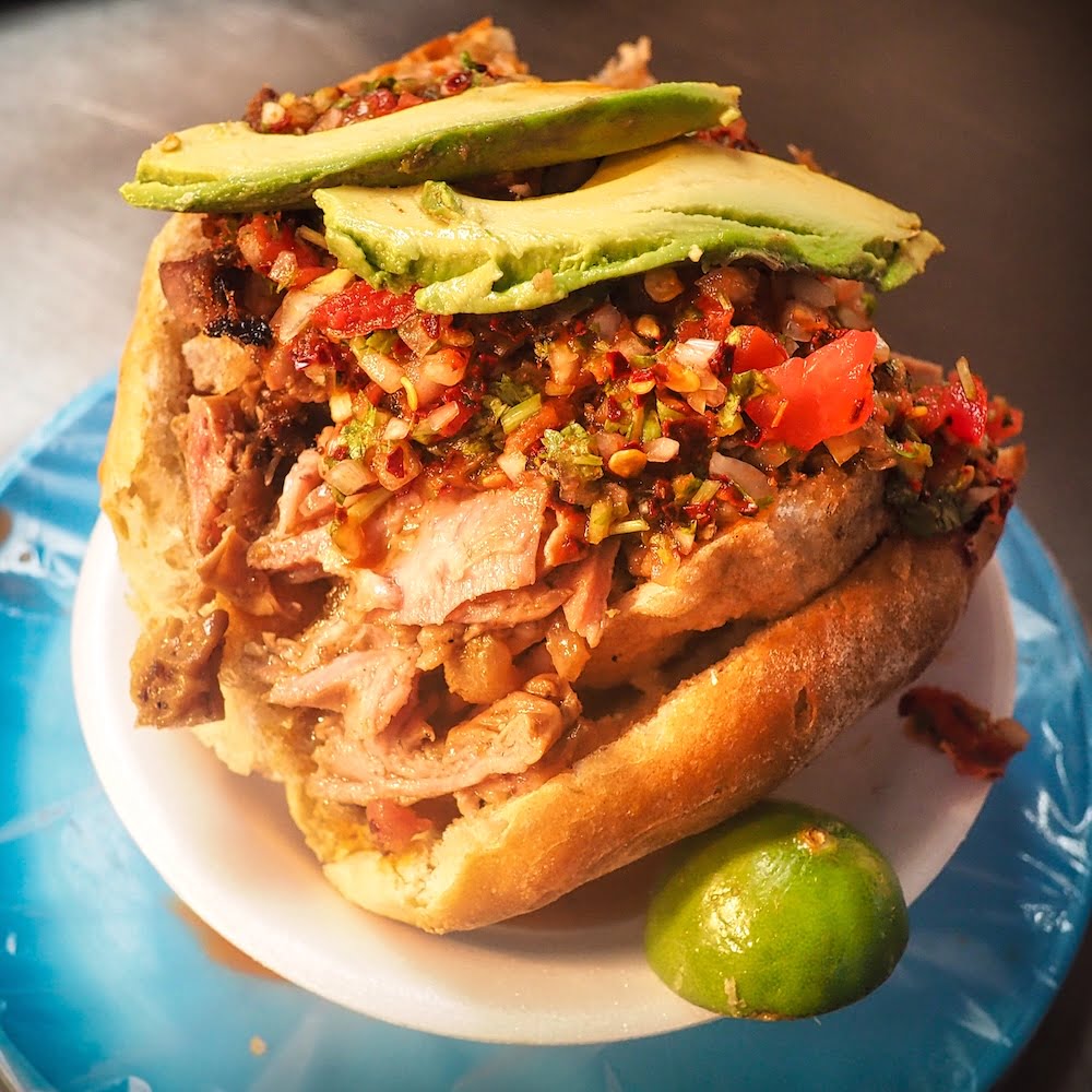 A bread roll filled with pork, chicharron, salsa and avocado