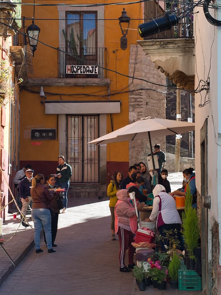 A mobile stall in a narrow street is surrounded by people