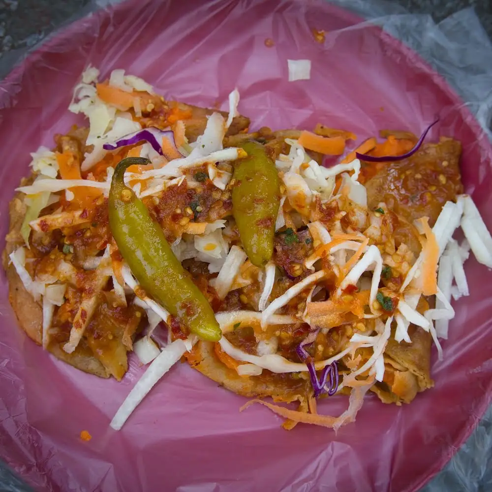 A plastic plate filled with tacos al vapor and smothered with salads and salsa