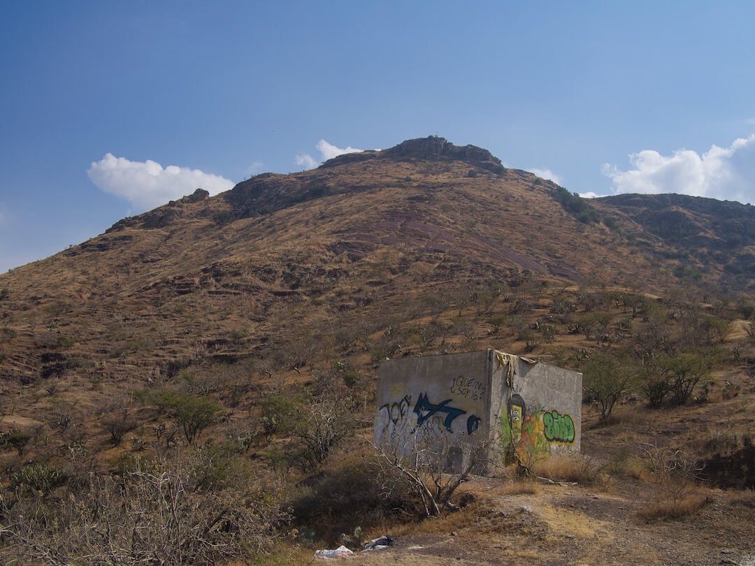 A white concrete hut covered in graffiti stands on a hillside