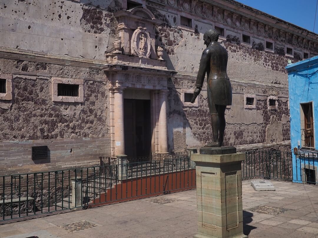 A bronze statue of a man stands outside a stone building