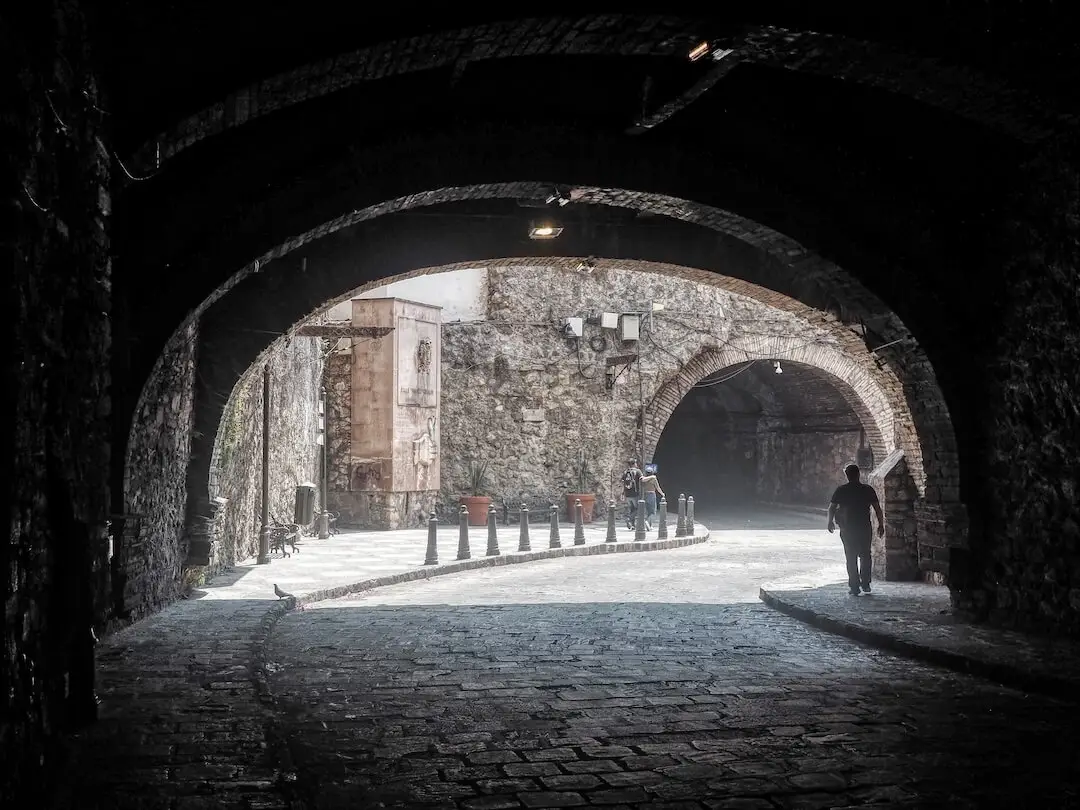 A cobbled road leads out of a stone tunnel