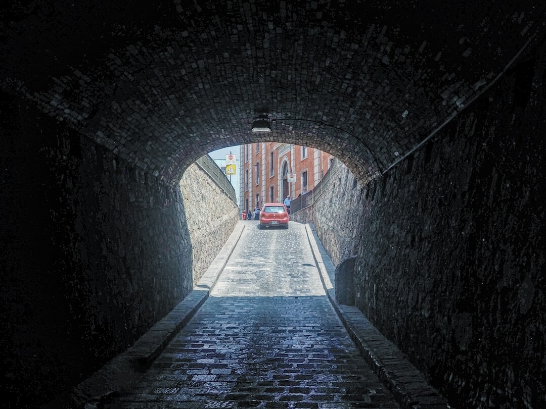 A red car in the distance is driven out of a stone tunnel