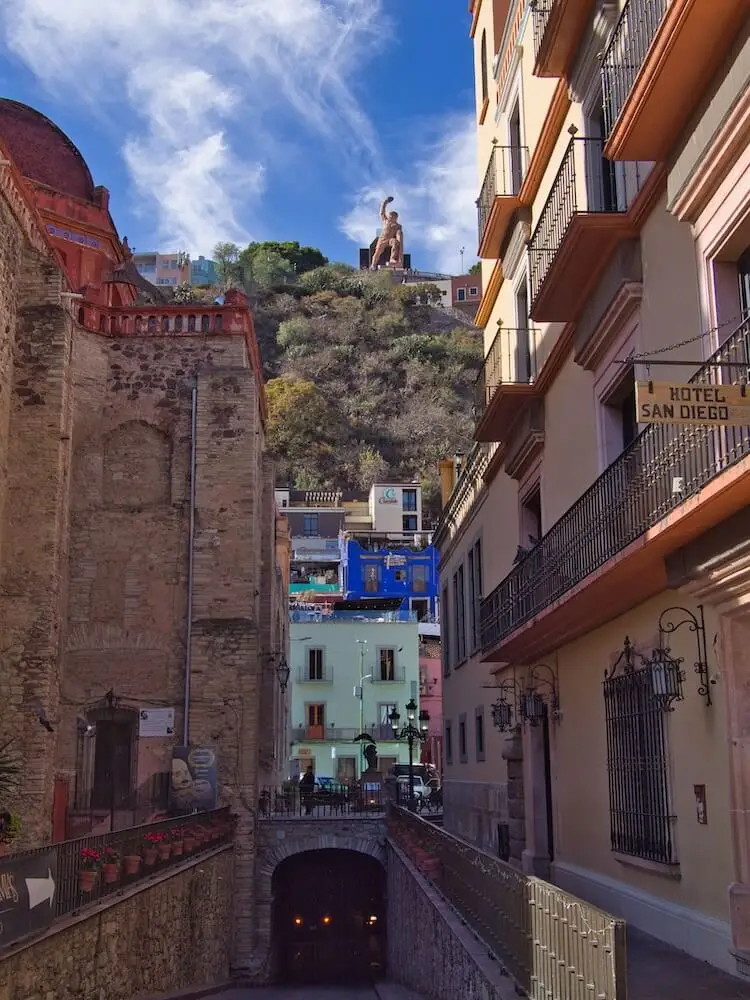 A statue on a hillside viewed in between buildings on a narrow street