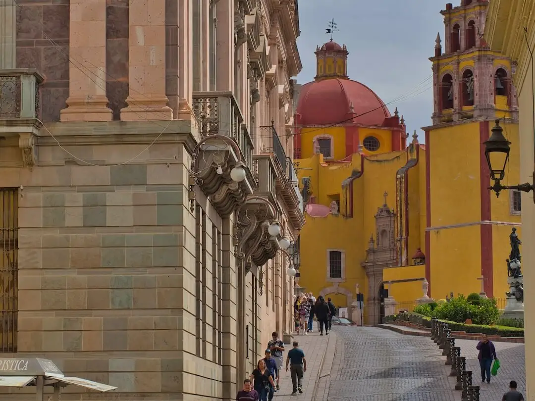 A pillared building in the foreground with a yellow church and red domed roof in the background
