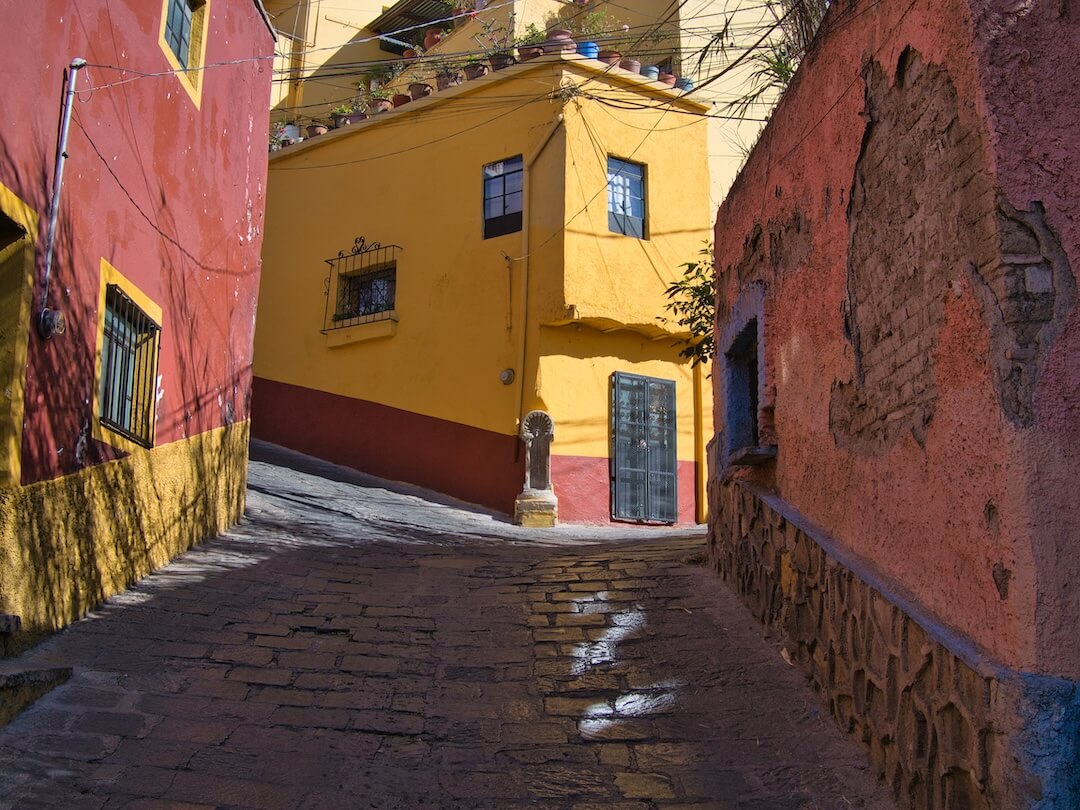 A hilly cobbled street with yellow and pink coloured houses either side