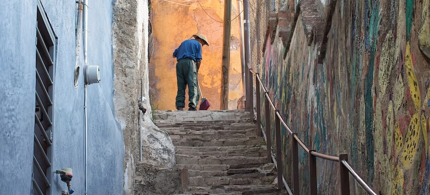 A Walking Tour of Guanjuato - a man sweeping the pavement in a narrow street at the the top of a set of steps