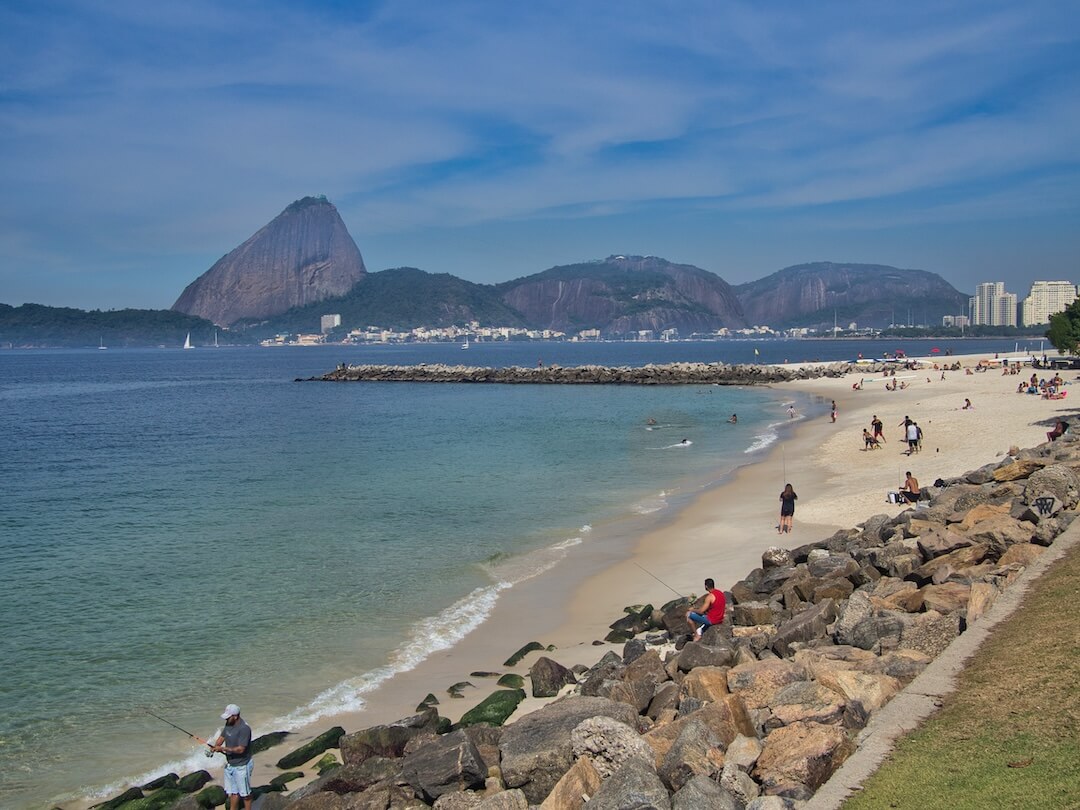 Large boulders on a beach, next to a bay, with Sugar Loaf in the background