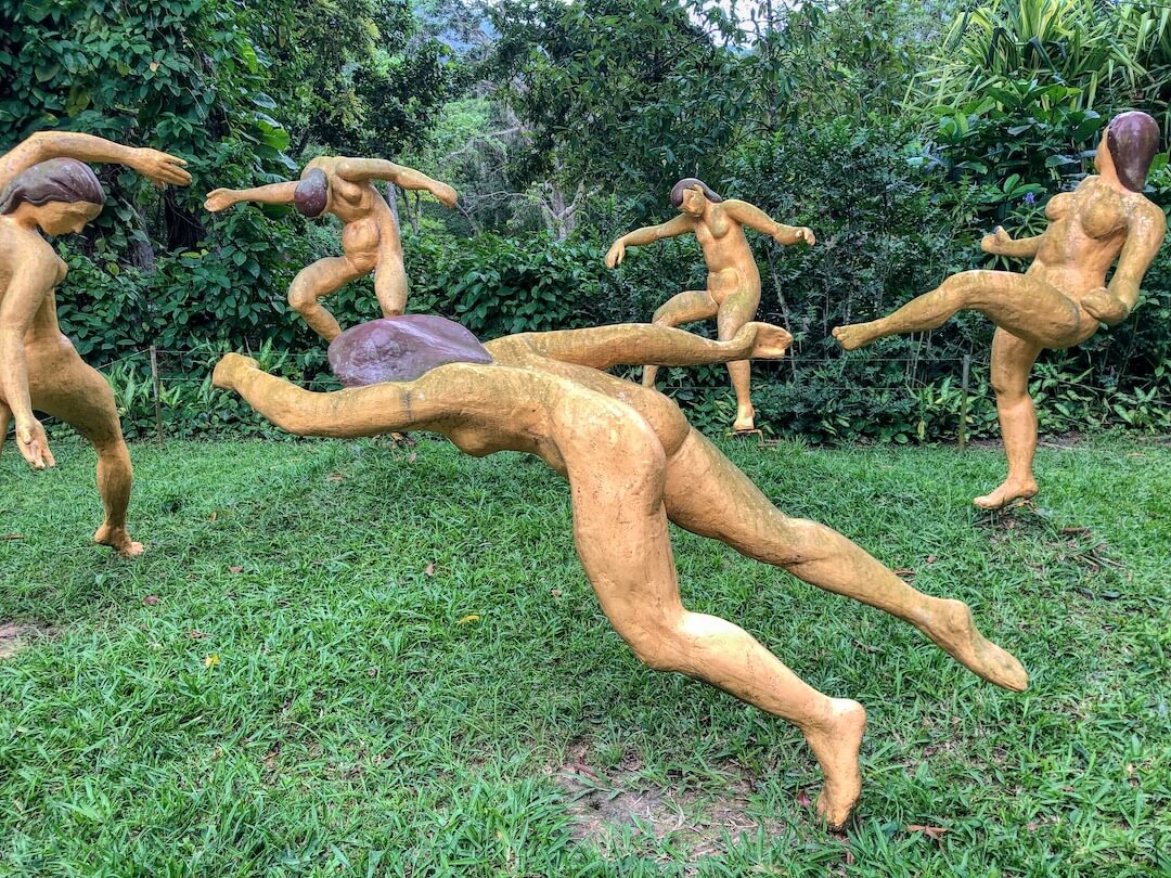 Naked statues playing football in a circle surrounded by vegetation