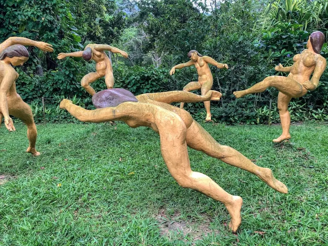 Naked statues playing football in a circle surrounded by vegetation