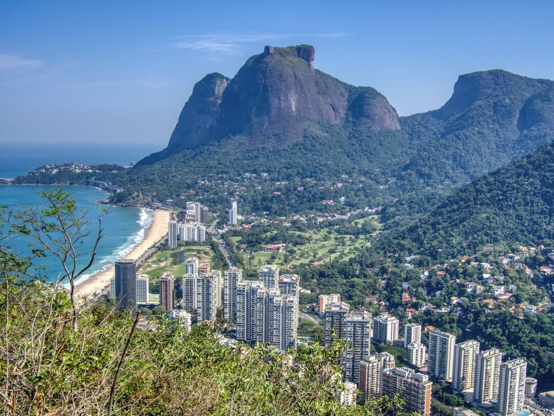 High-rise buildings surrounded by rainforest covered hills, beach and bay