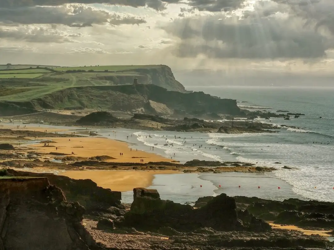 Bude - Main Beach - Cornwall A beach sits between a rocky headland in the foreground and a grassy headland behind
