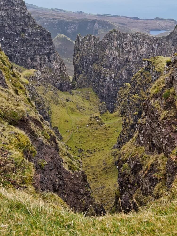 A steep gulley leads to a green plateau between walls of rock