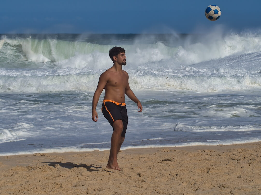 A man wearing shorts on a beach with large waves in the background